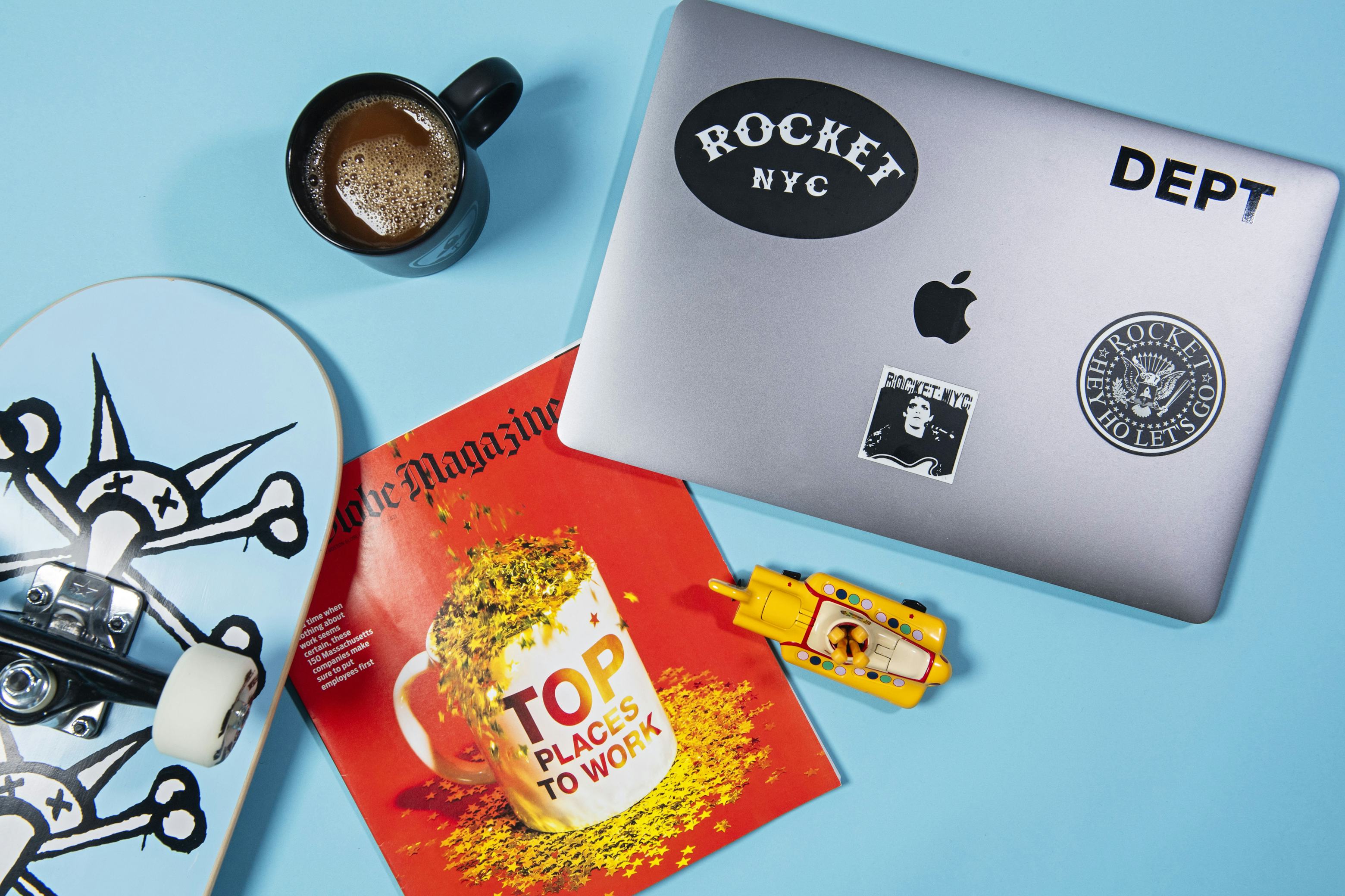 Desk with laptop, coffee, magazine, skateboard, and toy